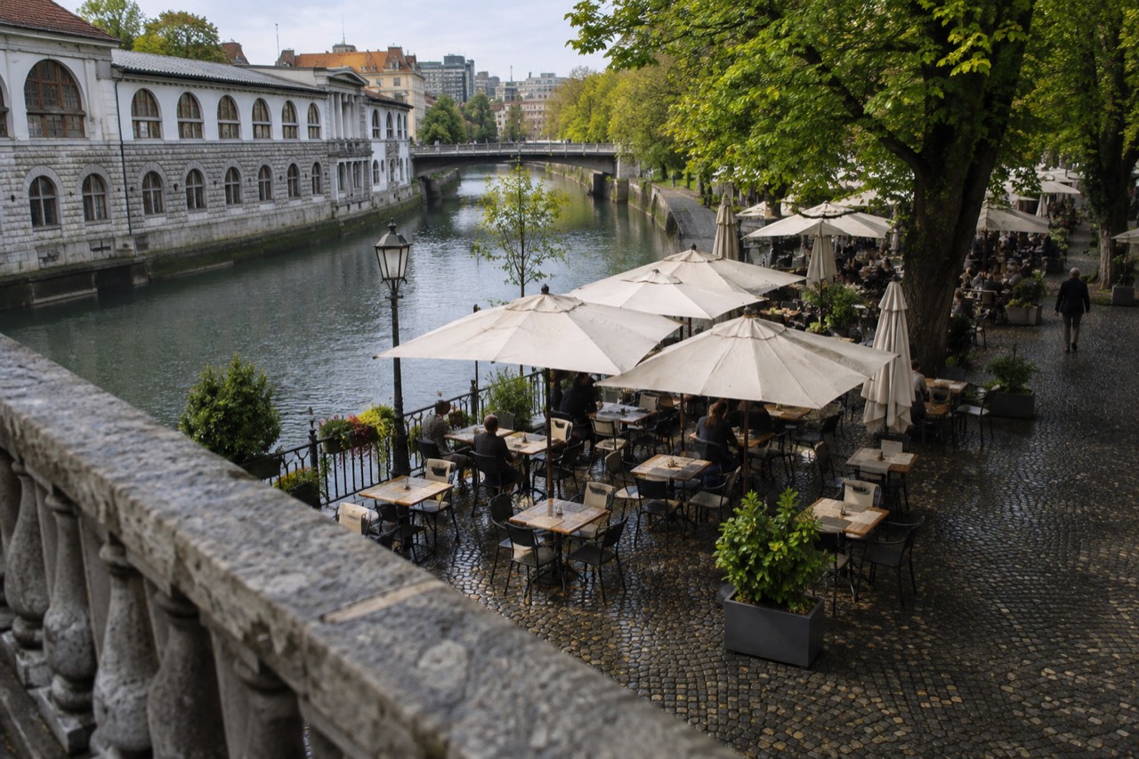 Morning café tables on a cobbled square beside the Ljubljanica river in Ljubljana