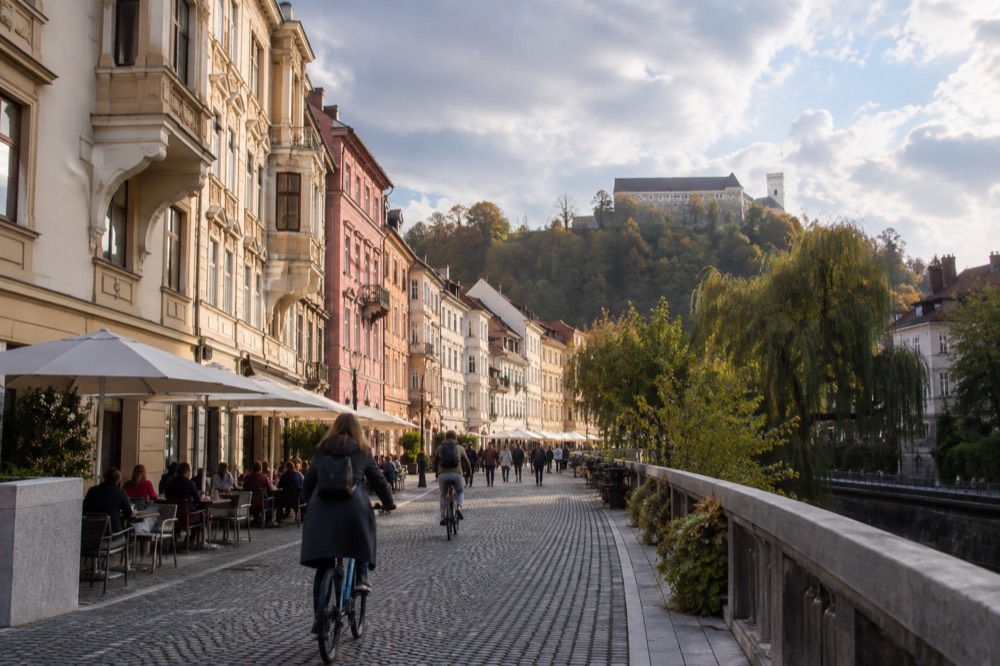 Cyclists and pedestrians on a car-free riverside street with cafe tables in a European old town