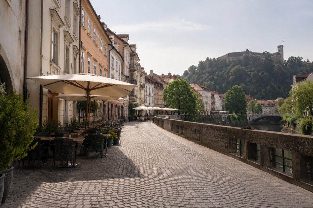 People-free view of a cobbled riverside street with cafe umbrellas in Ljubljana