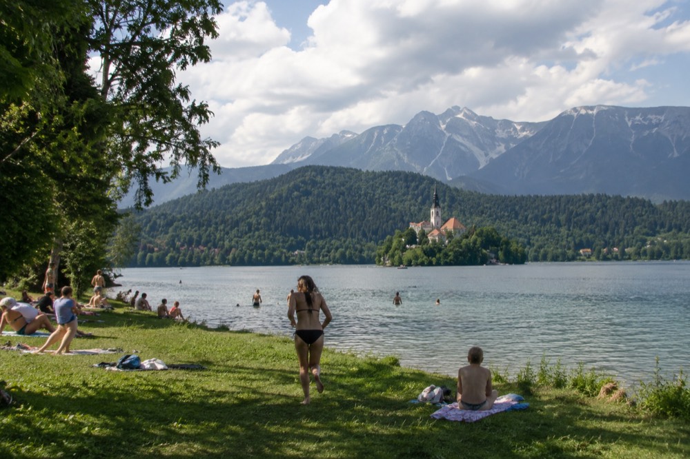 Swimmers and sunbathers on a grassy bank at the edge of Lake Bled in summer