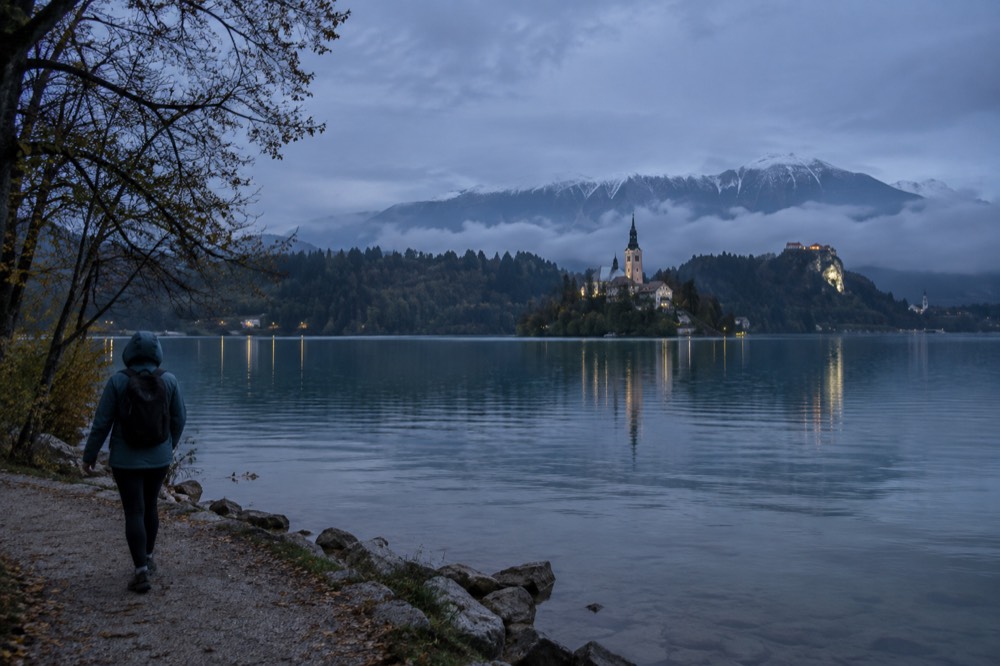 A hiker in a rain jacket on the shore path at Lake Bled under low cloud