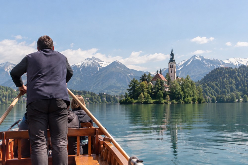 A wooden pletna boat approaching Bled Island under a clearing sky