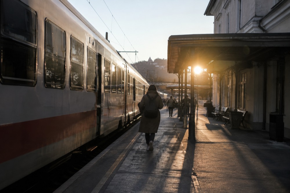A railway platform with a regional train and a station building under a clear sky.