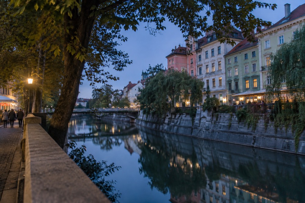 A riverside street of colourful historic buildings reflected in a calm river at dusk.