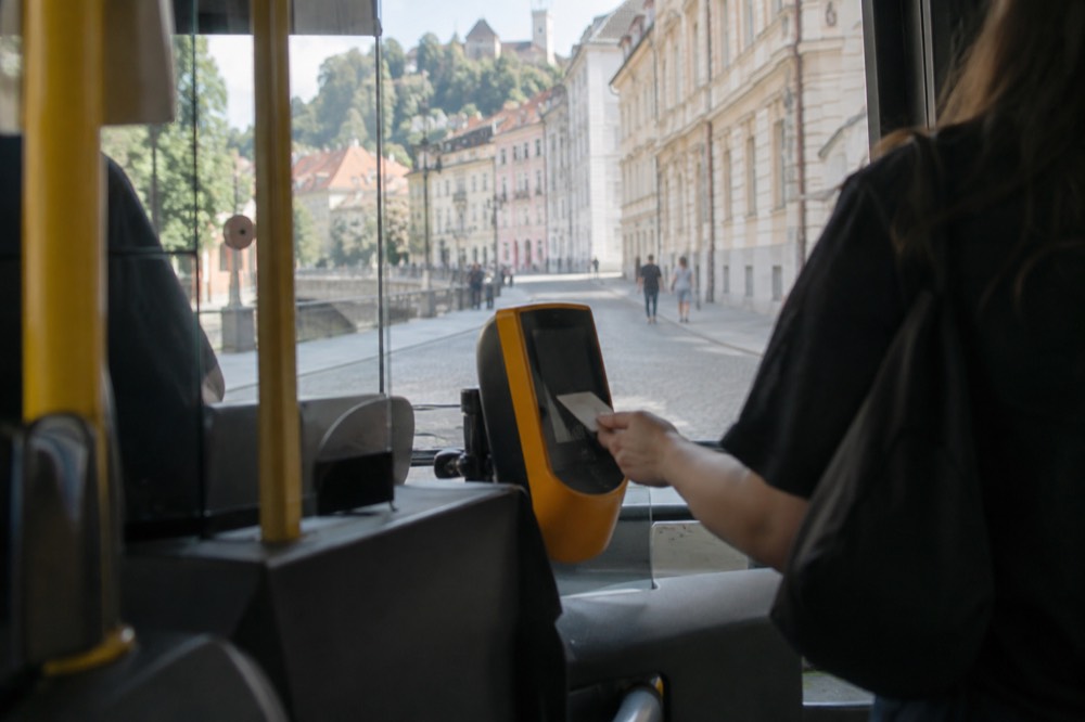 A hand tapping a contactless bank card on the validator at the front of a city bus