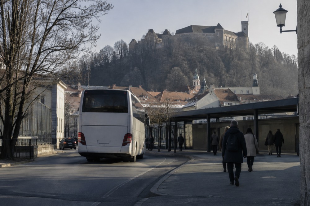 A coach departing the terminal with the castle hill and rooftops of Ljubljana in the background