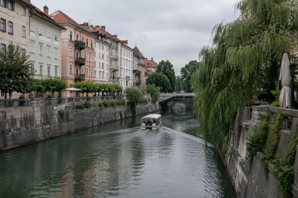 A small boat on the Ljubljanica river passing colourful riverside buildings