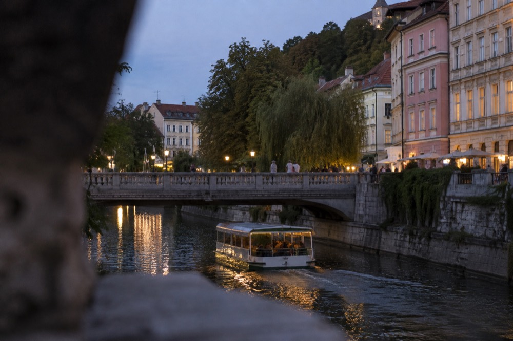A river boat passing under a Ljubljana bridge on a warm evening