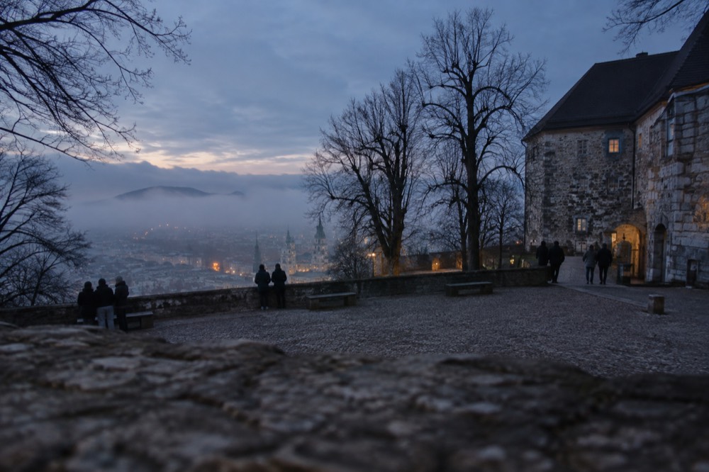 Fog lying over the Ljubljana old town rooftops with the castle hill faintly visible above the mist