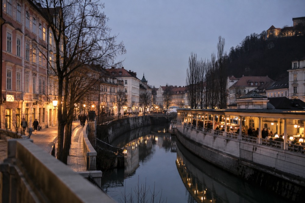 A covered riverside market building with winter stalls and lit windows in the early dusk