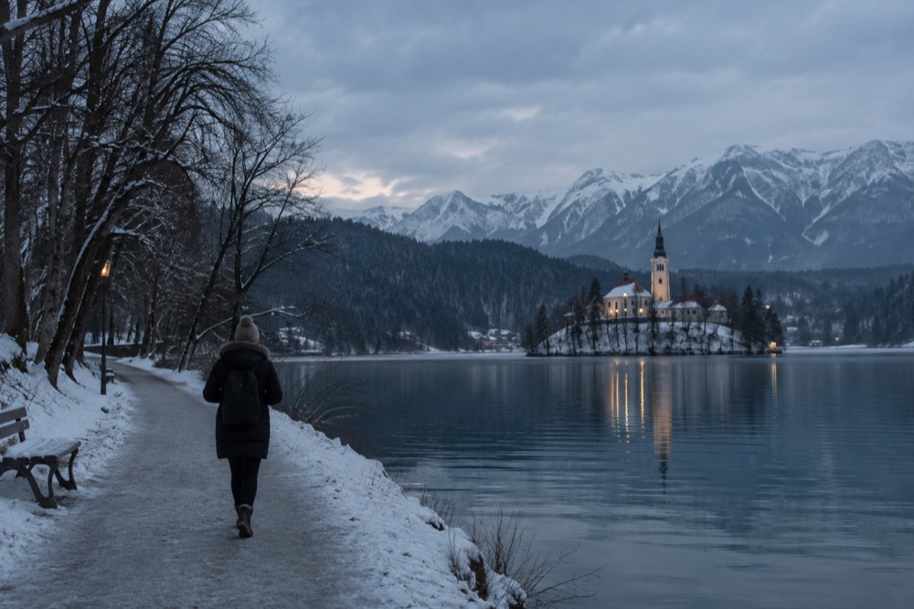 Lake Bled in winter with the island church and snowy forest shore under grey light