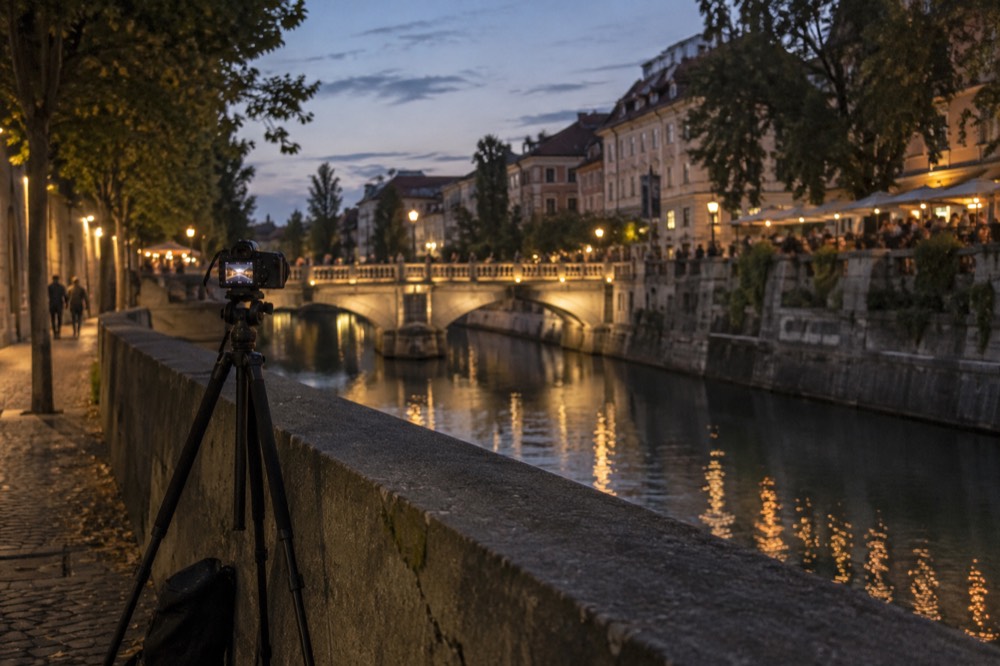 A tripod set up on a riverside path beside the Ljubljanica at dusk
