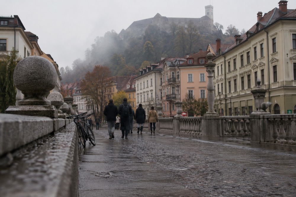 People walking across a bridge in the pedestrianised centre of Ljubljana with bicycles parked nearby