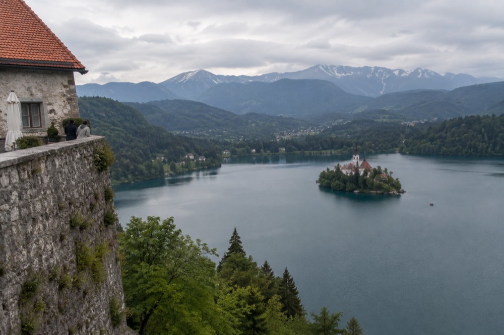 A stone castle wall high above a lake with an island church in the middle distance
