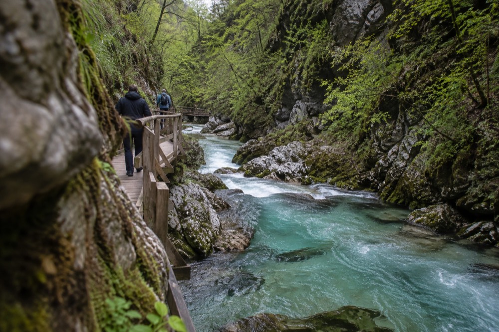 A wooden walkway along a narrow gorge with turquoise water rushing below