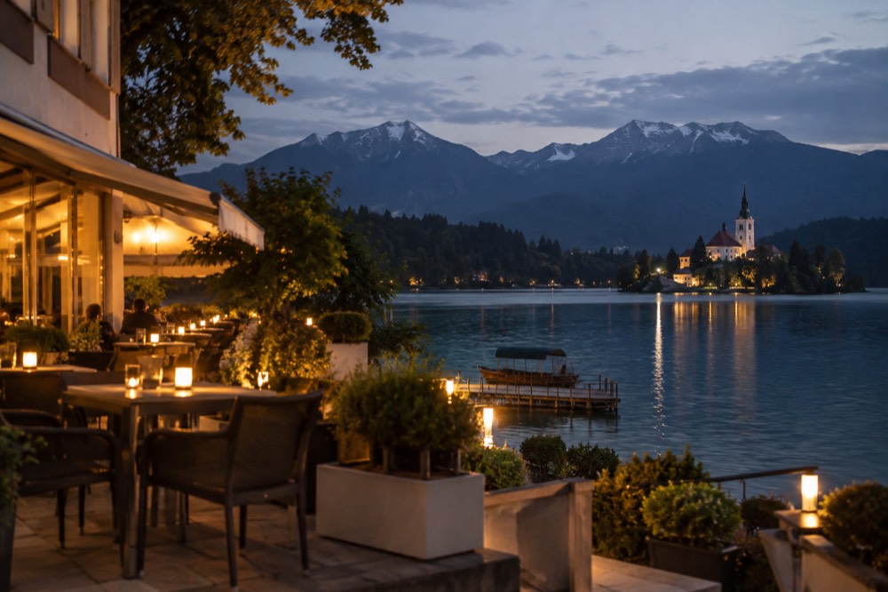 A lakeside hotel terrace at dusk with warm lights reflected at the water's edge