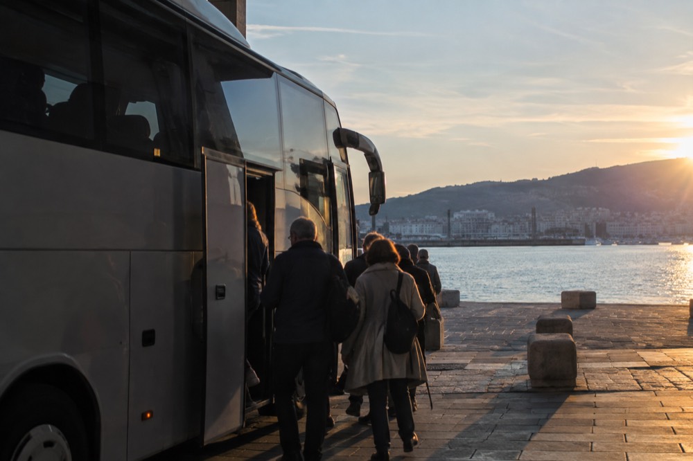 A coach parked at a station platform with passengers boarding