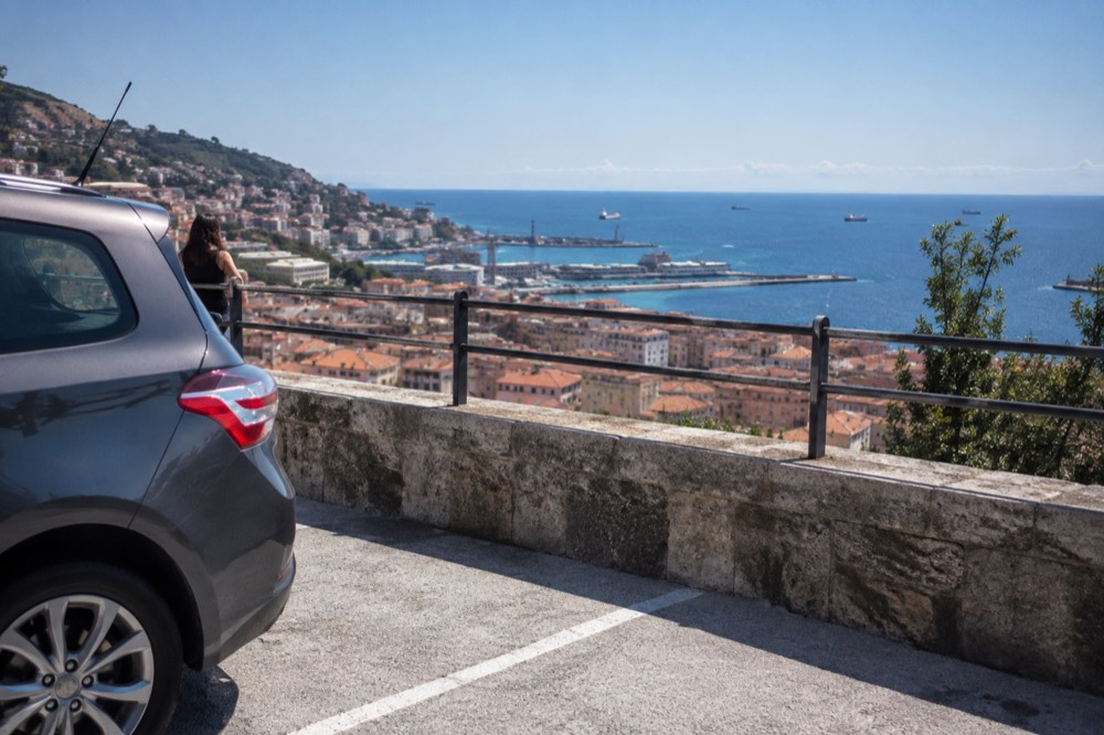 A car park terrace above a coastal town with terracotta roofs and a blue sea
