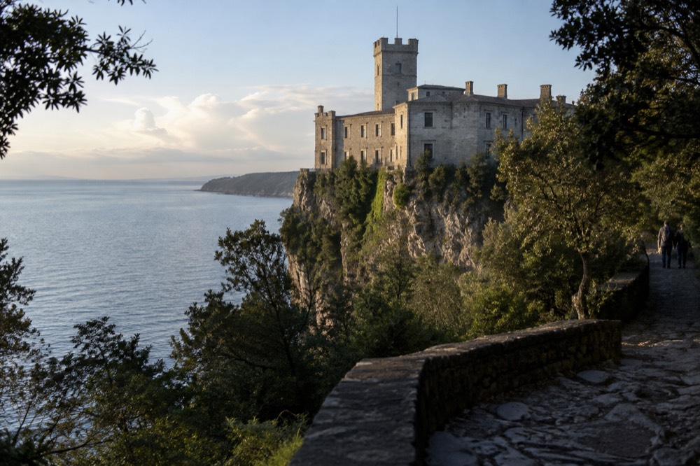 A stone castle built into a sheer cliff face above a wooded valley