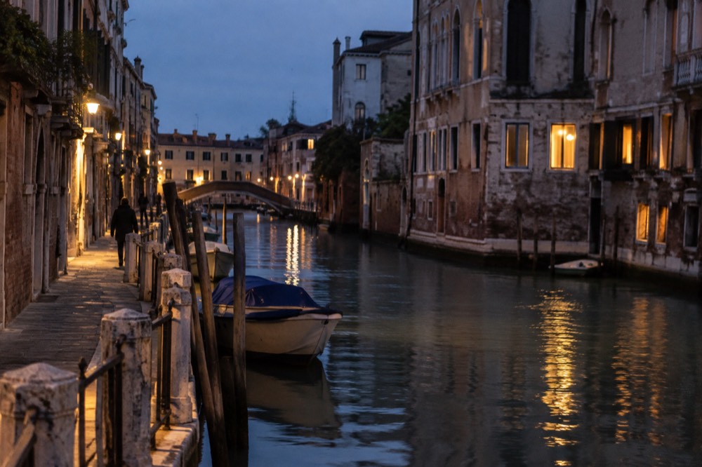 An evening canal in Venice with warm lights reflecting on still water