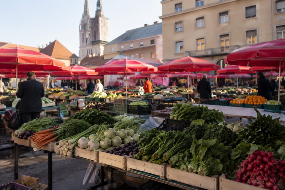Open air market stalls with fresh produce under red umbrellas on a city square