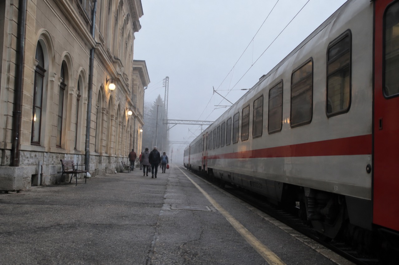 Railway platform with a train waiting beside a station building in Slovenia