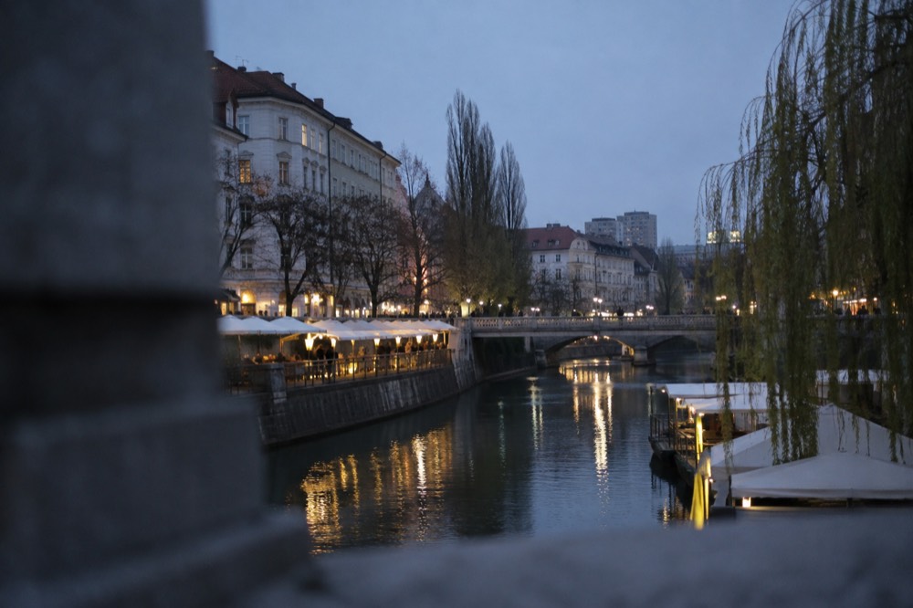 The Ljubljanica river in Ljubljana with riverside market stalls and bridges in soft morning light