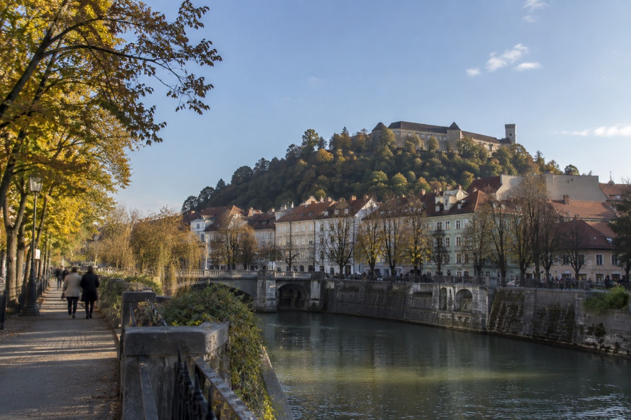 Pastel buildings along the Ljubljanica river in Ljubljana with the castle hill rising behind