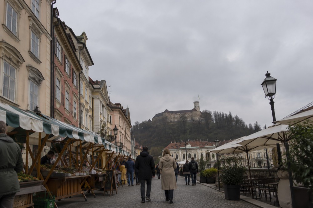 Outdoor food stalls with striped canopies beside a riverside market square in Ljubljana