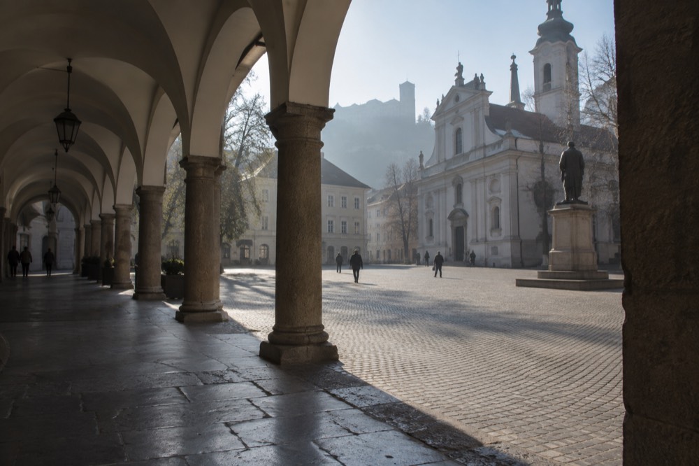 A wide pedestrian square with a church facade and a statue under morning light