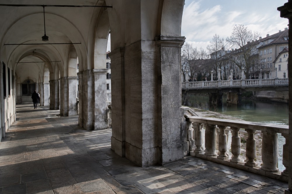 A stone bridge with columns and balustrades over a green river