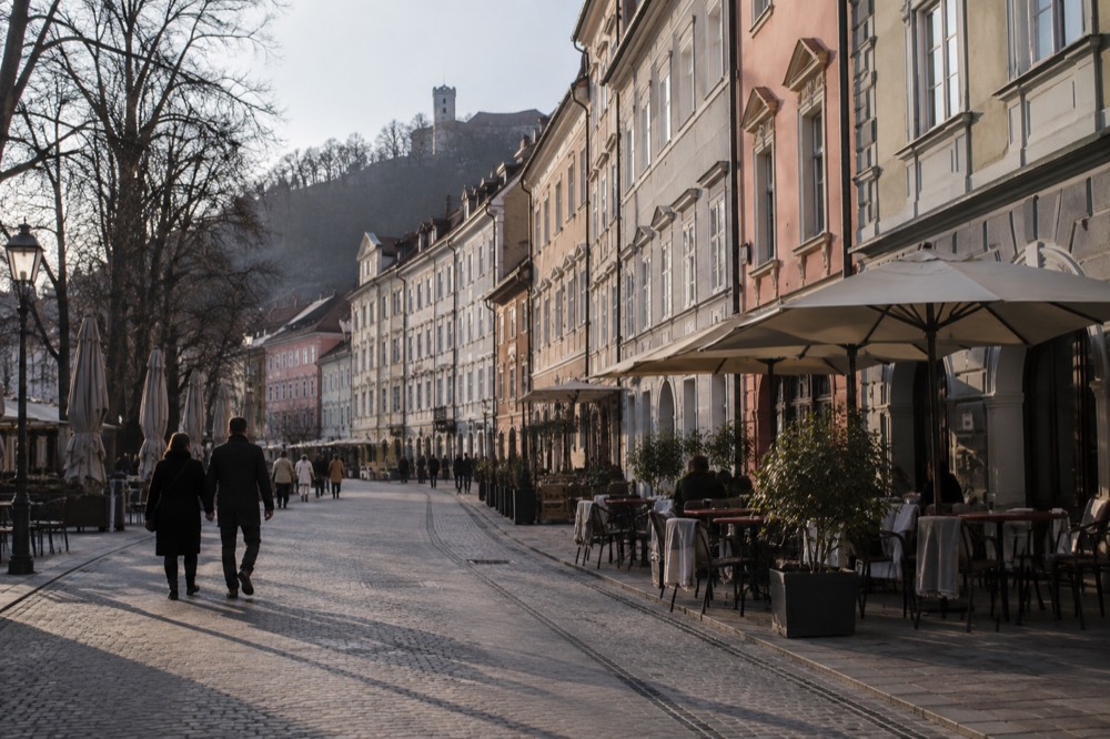 A wide pedestrian street lined with colourful building facades and cafe tables in a European old town