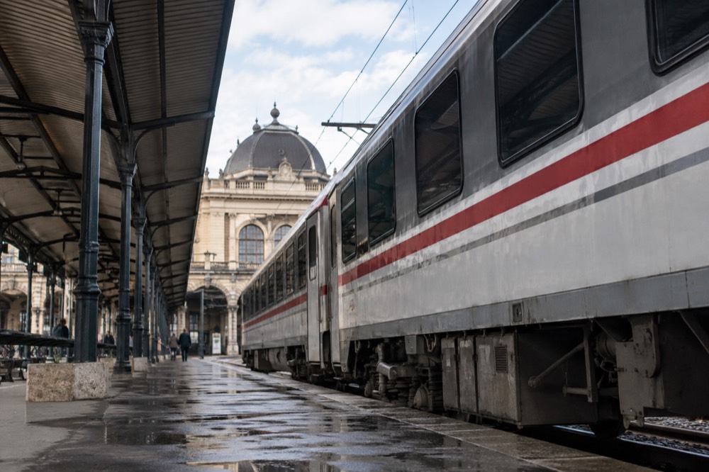 A passenger train standing at a platform with Zagreb station architecture visible behind it