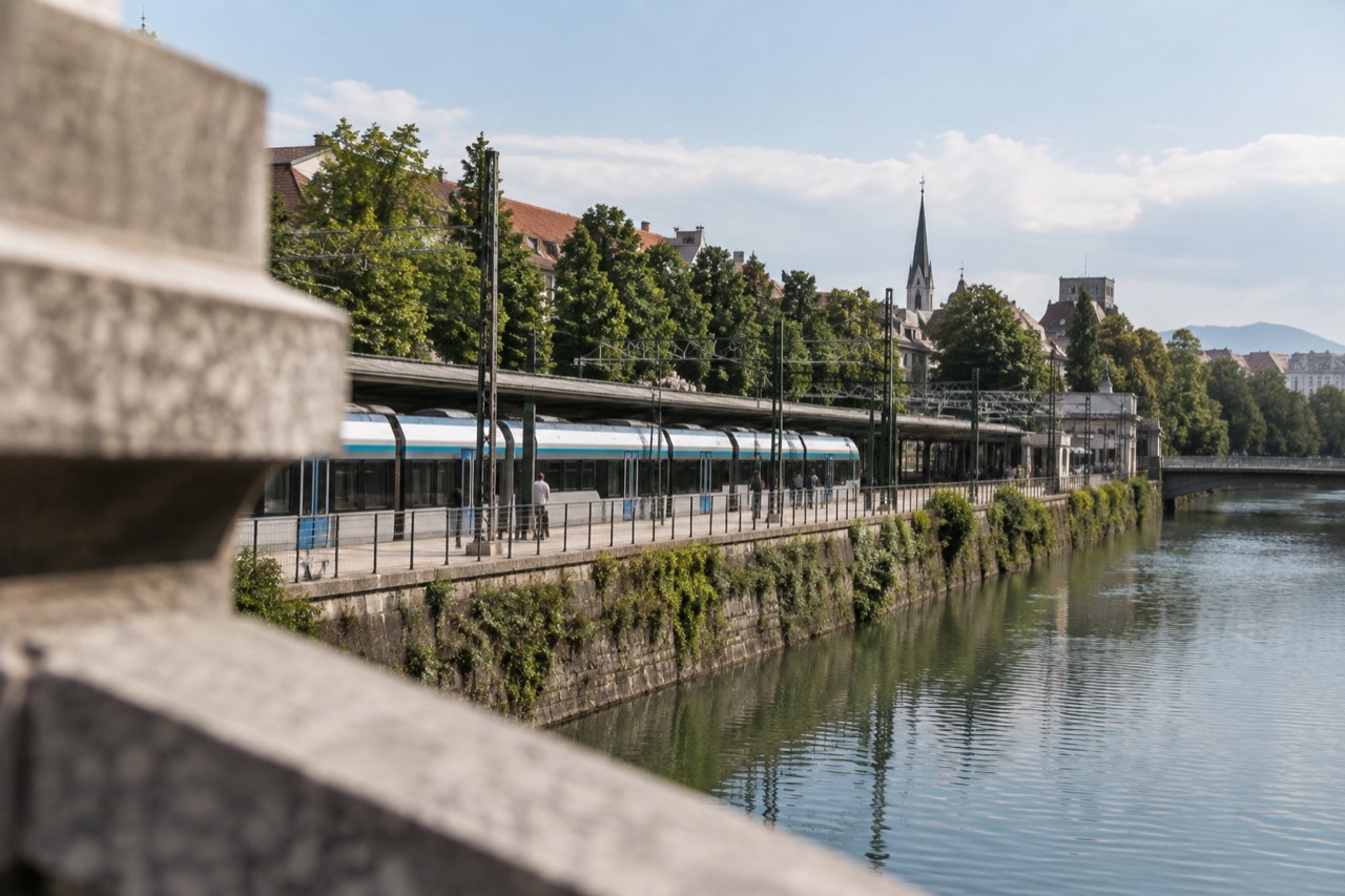 A Slovenian passenger train at a platform beside the Ljubljanica river in Ljubljana