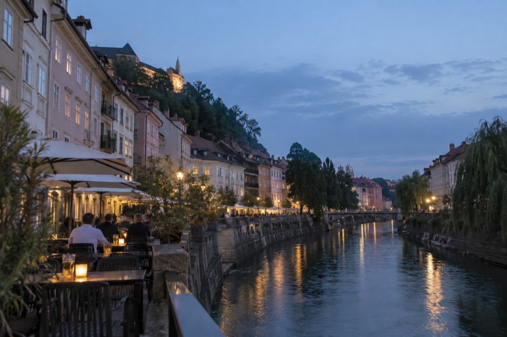 Outdoor tables beside a river in a European old town at dusk