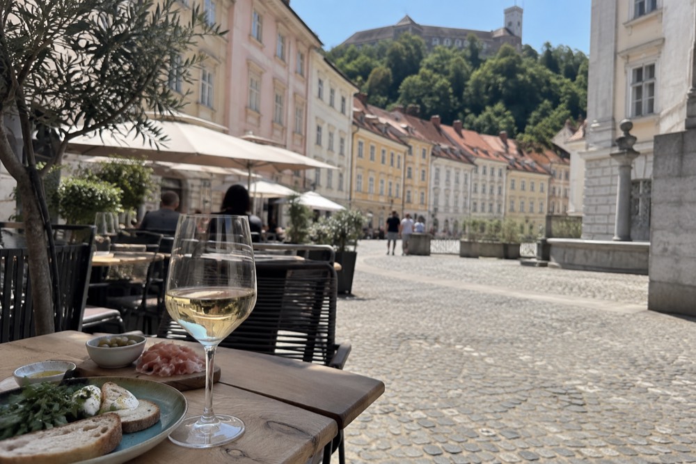 Glass of white wine and small plates on a café table in a city square