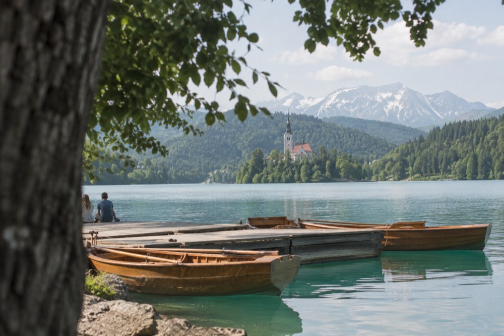 Small group of wooden boats moored at a pier on Lake Bled with forested hills behind
