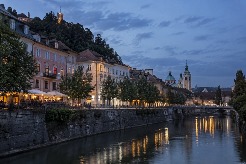 Ljubljana street and cathedral spire seen across the river at dusk