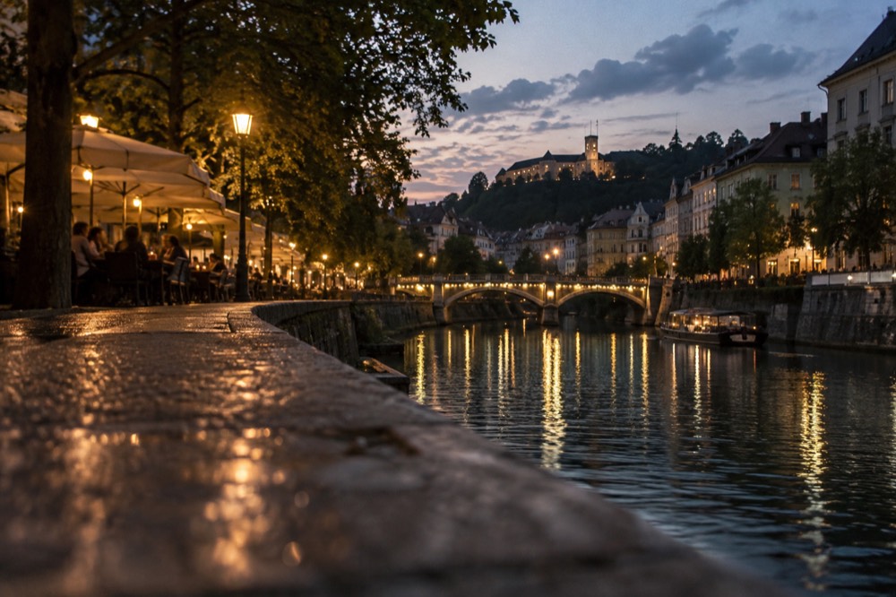Riverside promenade at dusk with lit bridges and a hilltop castle silhouette