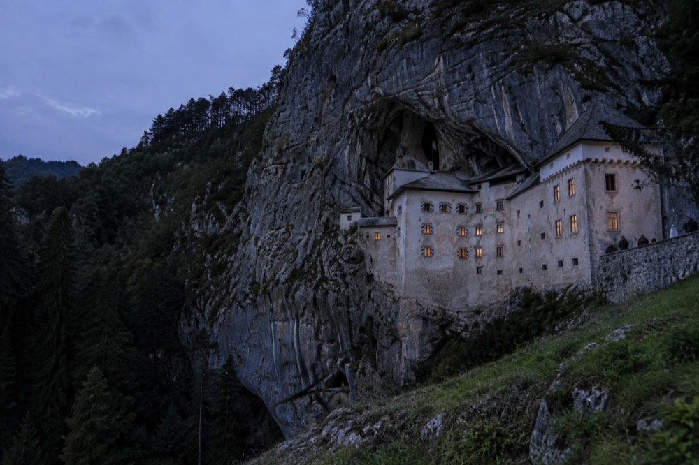 The cliff face of Predjama Castle built into a rocky overhang above forest