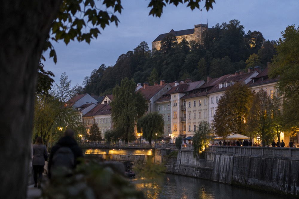 Pastel buildings along the Ljubljanica river with the castle hill rising behind them